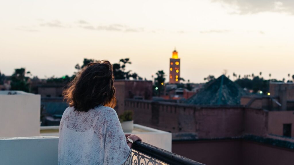 Voyageuse sur une terrasse de Marrakech au coucher du soleil, la Koutoubia au loin